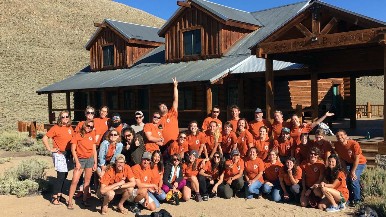 People wearing orange shirts pose in front of cabin.