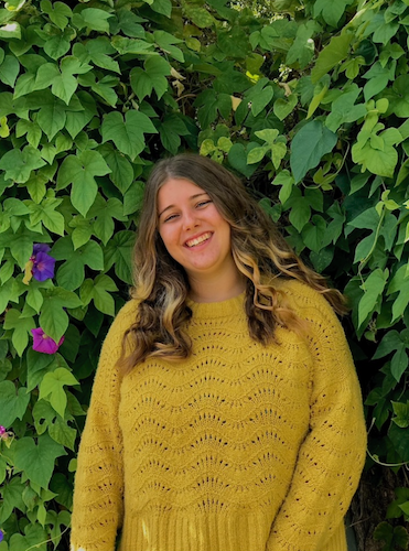 A student smiling in front of beautiful green leaves