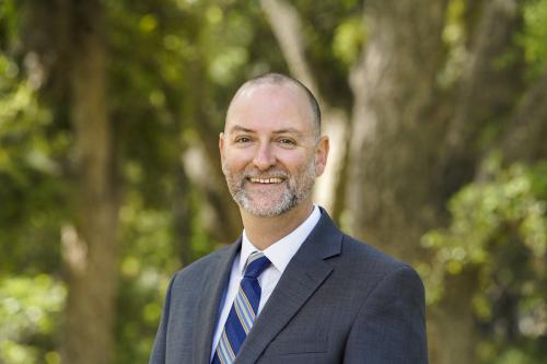 Robert Penman, UC Davis admissions director, smiling in front of beautiful green trees.