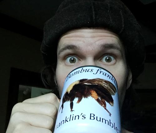 Man drinks from coffee cup decorated with bumblebee image.