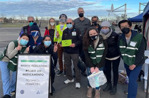 Workers at vaccine clinic pose for photo in front of sign.