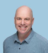 Headshot — smiling bald man in light-blue polo against pale blue background