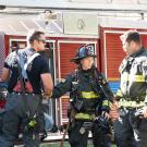 Three firefighters, in gear, in front of firetruck