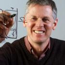 Professor Andy Albrecht, facing camera, through translucent "chalk" board.