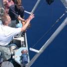 Photo of man on boat gesturing toward lake as people watch.