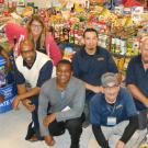 Mail Services personnel, kneeling in front of lots and lots of donated food.