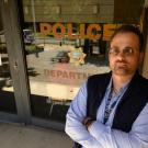 James Bronson stands outside police building, "Police" sign on window, in background.