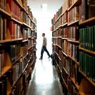 Library stacks, with a patron walking by.