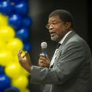 Walter Robinson speaks from podium, with backdrop of blue and gold balloons.