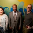 Facing the camera and standing in a row in front of a blue, green and yellow colored wall with a UC Davis logo stands, from left to right, Julia Lee, Chancellor Gary S. May and Dustin Lower.