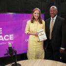 Two people on 'Face to Face' set; woman in yellow holds certificate, man in suit.