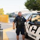 Campus police officer standing beside UC Davis patrol car on sunny sidewalk