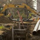 A big trench on the Quad with large underground pipes and a yellow excavator in the background