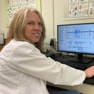 Woman dressed in lab coat looking at data on a computer screen