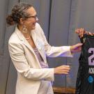 Two women smiling hold a black No.26 basketball jersey on stage.
