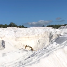 A quarry of bright white sand under a deep blue sky. An excavating machine can be seen in the distant center. 