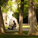 A photograph of a painter working on a canvas while near the statue of the Eye on Mrak sculpture.