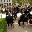 Members of a symphony play music near the Eye on Mrak Egghead sculpture as a large crowd looks on.