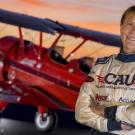 A woman in a flight suit stands in front of a red biplane.