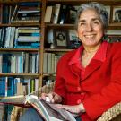 Brenda Schildgen in her book-lined library sitting with a book 