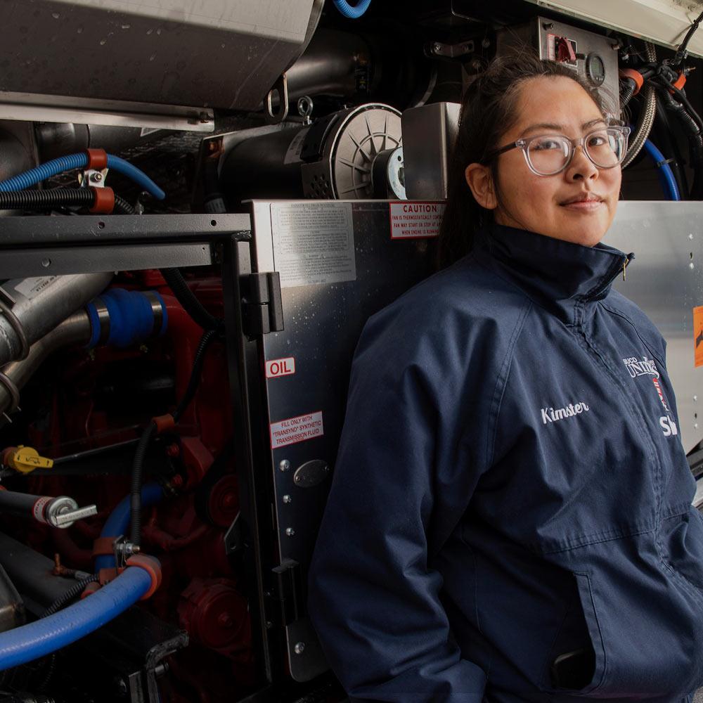 A female student leans against a bunch of technological equipment