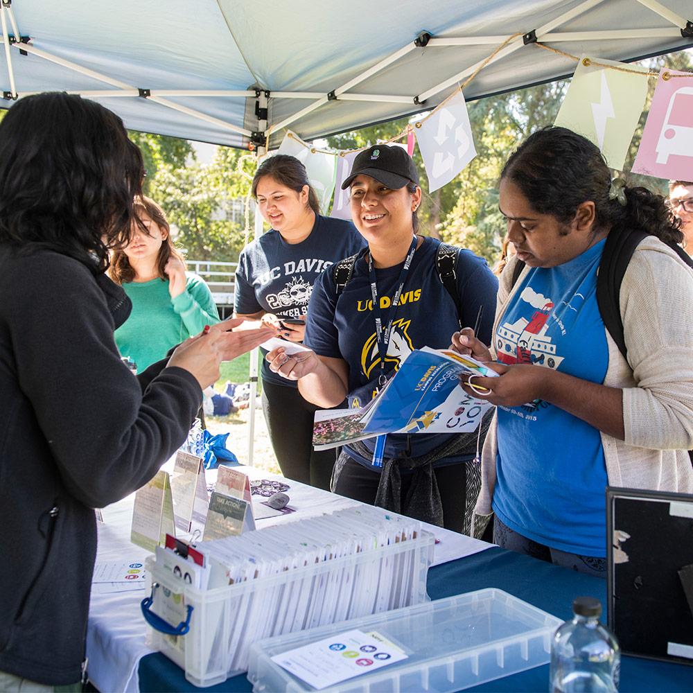 students receiving health information outdoors at a table in a tent