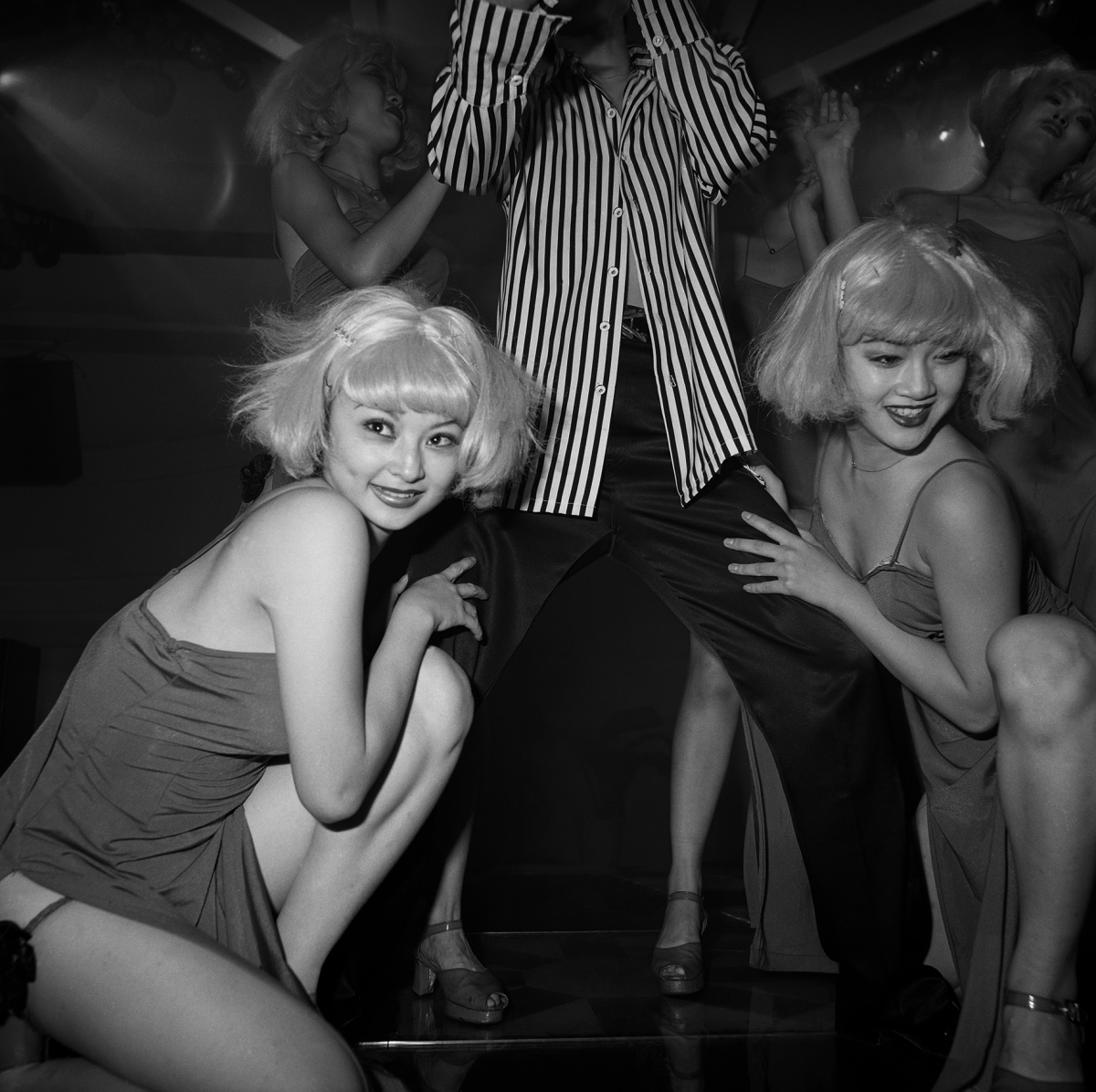 Two women kneeling on either side of a man on a dancefloor. Zheng dancers in a nightclub, beijing, 1999.