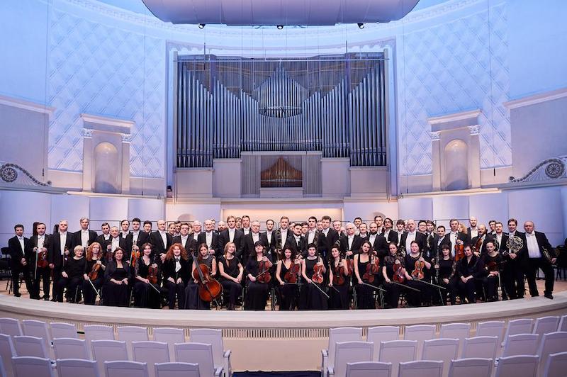 The Russian national Orchestra on stage in formal wear with their instruments.